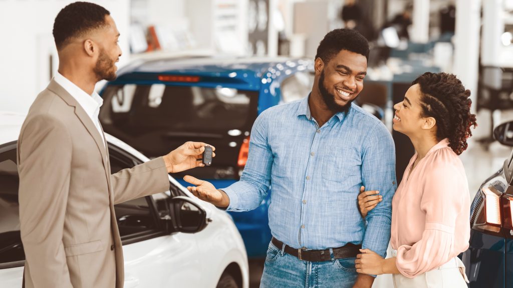 Salesperson giving car keys to happy couple in showroom.